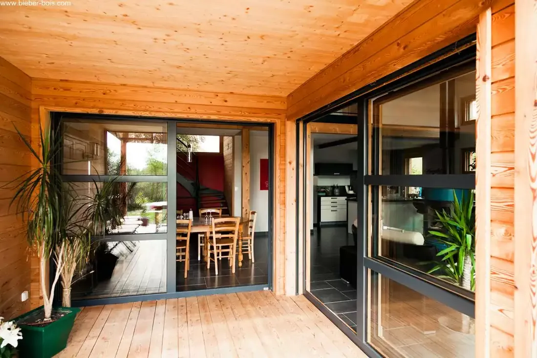 Baie vitrée coulissante à levage avec profilés mixtes bois et aluminium, s'ouvrant sur une terrasse en bois d'une maison moderne à Pau