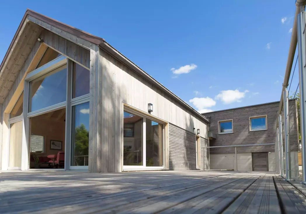 Baie vitrée d'angle en bois et fenêtres coulissantes, intégrées à une façade de maison moderne avec bardage bois et terrasse panoramique à Pau