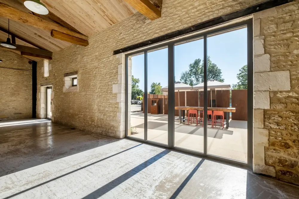 Grande baie vitrée coulissante en aluminium gris, intégrée dans une rénovation de bâtiment en pierres apparentes à Pau