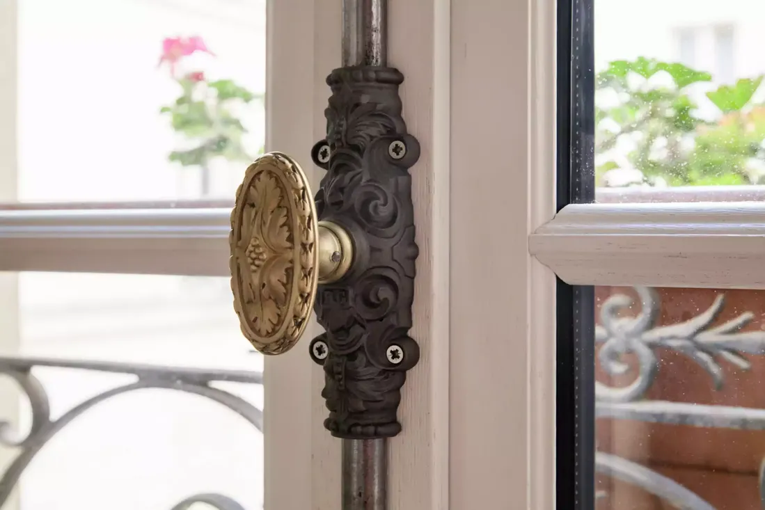 Gros plan sur une crémone décorative en laiton vieilli sur une fenêtre en bois, typique des rénovations de style ancien au centre historique de Pau