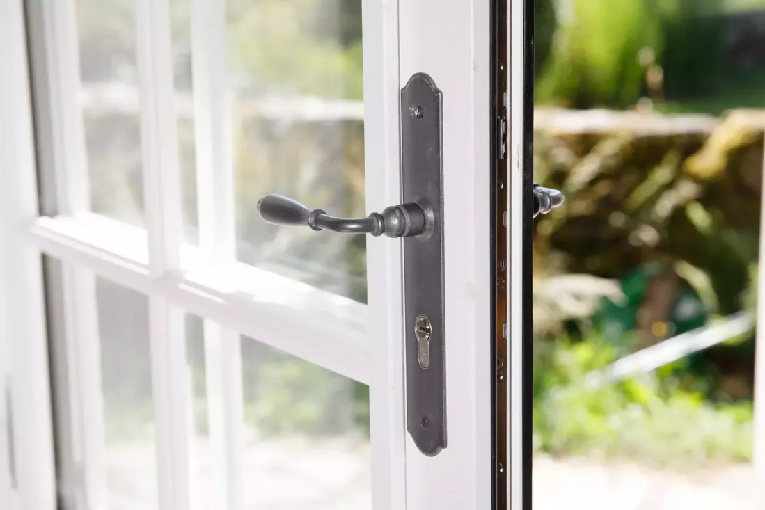 Gros plan sur la poignée de style ancien et la serrure d'une porte-fenêtre en bois blanc à petits carreaux, renforçant la sécurité à Pau