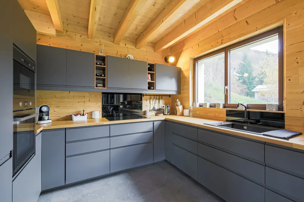 Fenêtre aluminium de cuisine dans un intérieur style chalet avec murs et plafond en bois, offrant une vue sur la nature