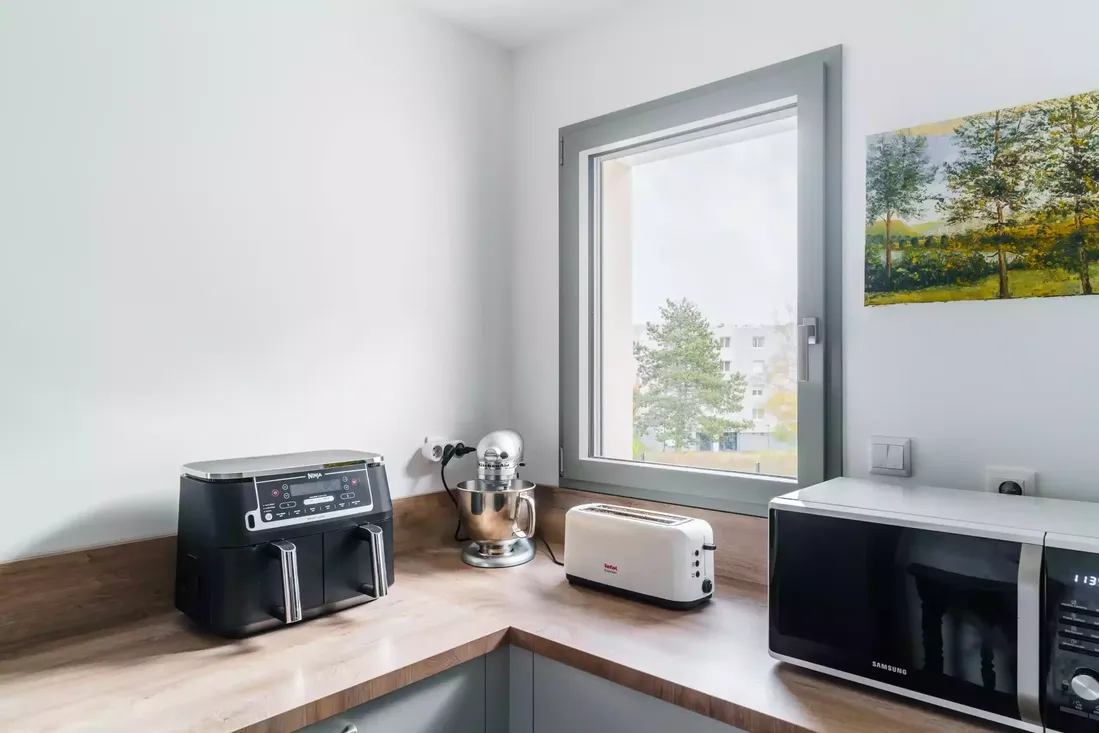 Fenêtre en aluminium gris clair dans une cuisine moderne, apportant de la lumière au plan de travail, avec vue sur un environnement urbain