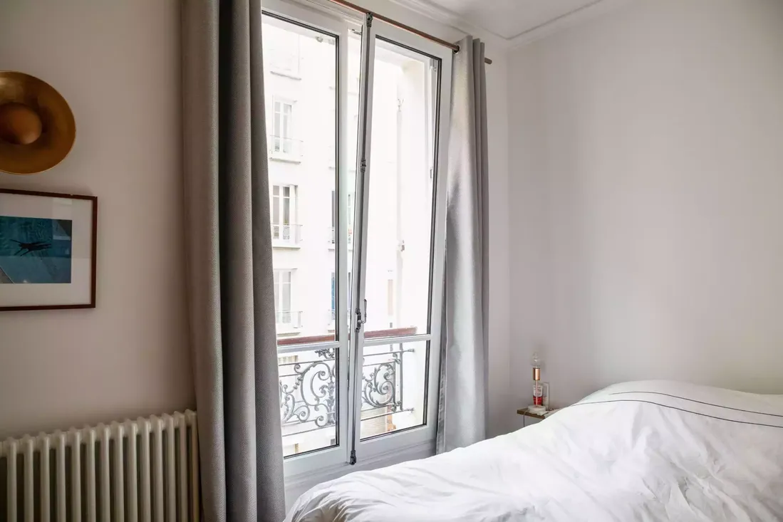 Fenêtre en bois blanche à double battant avec balconnet en fer forgé, installée dans une chambre d'appartement en centre-ville de Pau