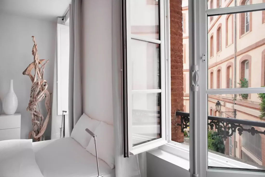 Fenêtre en bois blanc à la française, à double battant, installée dans une chambre moderne avec vue sur une rue de briques typique du centre-ville