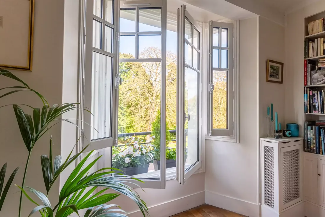 Fenêtre en bois blanche à double battant et petits carreaux, maximisant la lumière naturelle dans un salon de lecture
