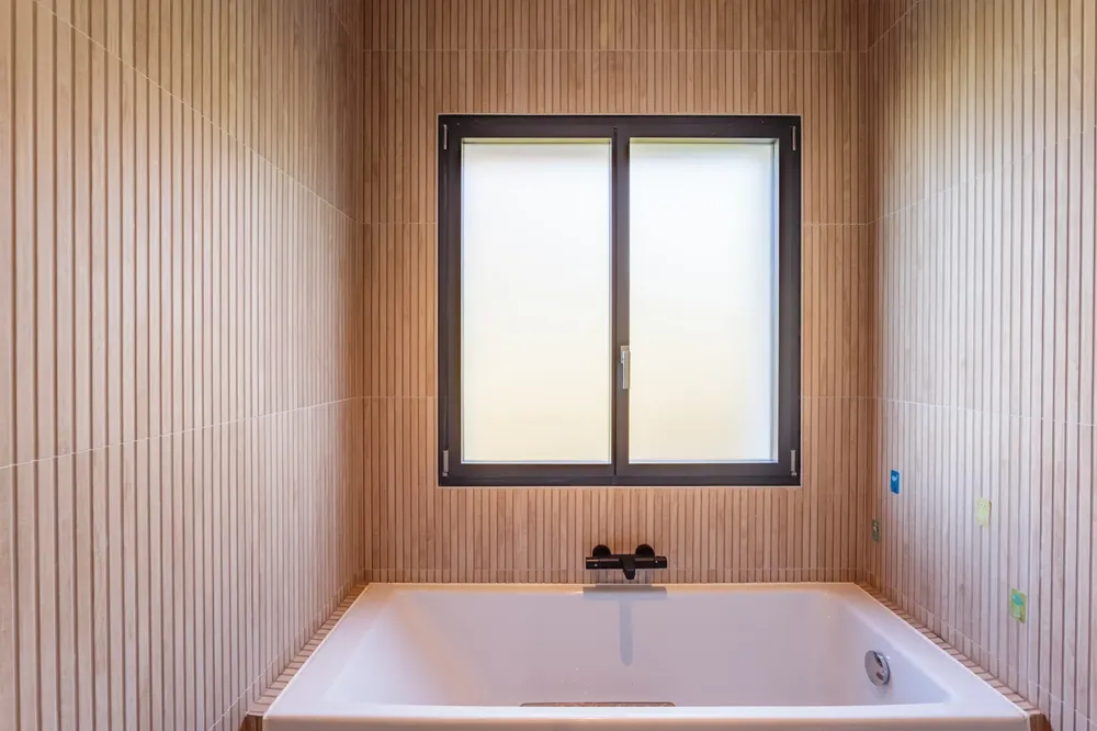 Fenêtre coulissante en aluminium noir avec vitrage opaque, installée au-dessus d'une baignoire dans une salle de bain moderne à Pau