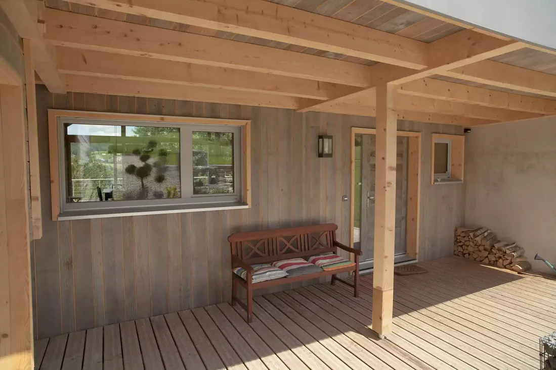Fenêtre coulissante avec cadre en bois et profilé gris, intégrée à la façade d'un chalet moderne avec terrasse couverte en bois à Pau