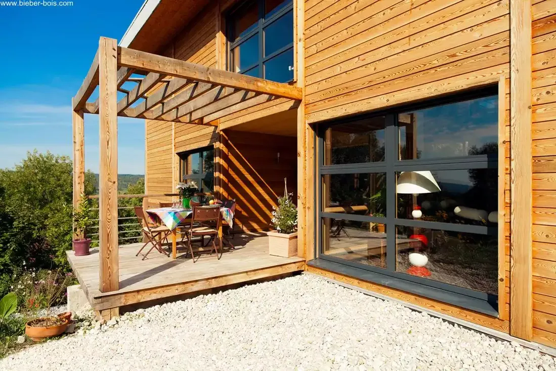 Grande fenêtre fixe avec profilés en aluminium et cadre en bois, intégrée à une façade de maison moderne en bois lambrissé avec terrasse à Pau