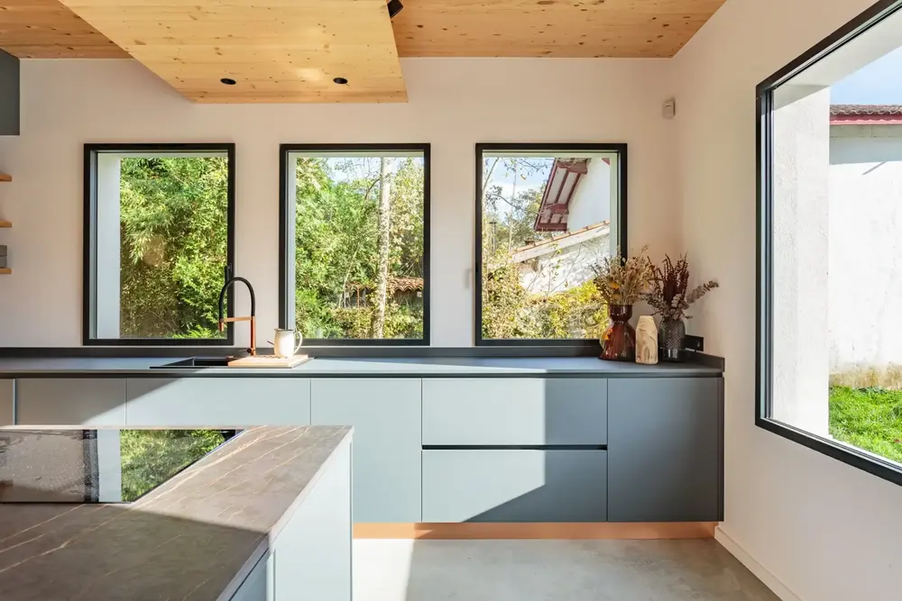 Trois fenêtres aluminium bandeau noires au-dessus de l'évier, intégrant une cuisine contemporaine avec plafond bois à Pau
