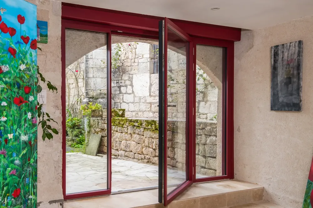 Porte-fenêtre en aluminium rouge, style rénovation, avec ouverture oscillo-battante, intégrée dans une façade en pierre à Pau