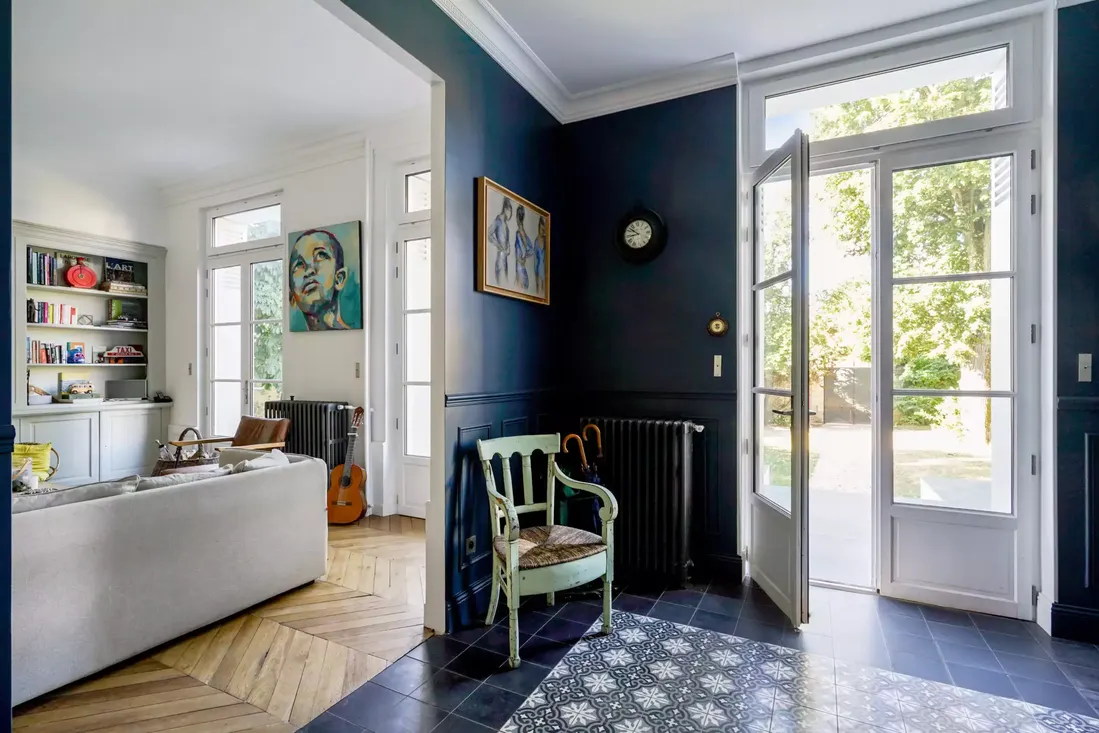 Grande porte-fenêtre en bois blanc à petits carreaux, servant de sas d'entrée dans une maison ancienne rénovée avec des murs bleu marine à Pau