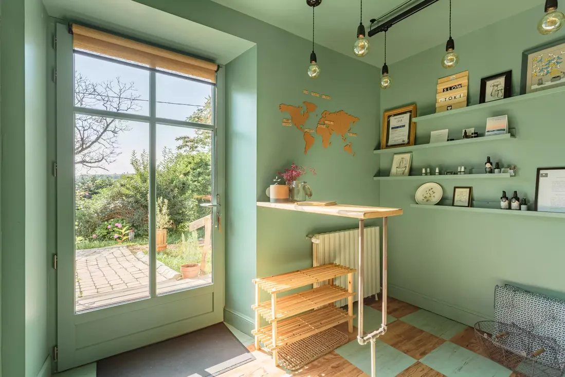 Porte-fenêtre en bois couleur vert pastel, installée dans un petit local commercial ou bureau, offrant un accès direct au jardin à Pau