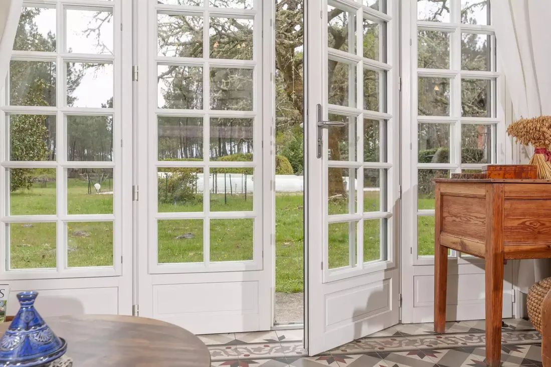 Ensemble de portes-fenêtres en bois blanc à petits carreaux, avec poignée en inox, s'ouvrant sur le jardin d'une propriété à Pau