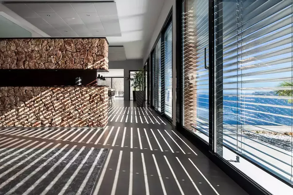 Brise-Soleil Orientable à lames en aluminium, créant des effets d'ombre et de lumière dans un intérieur moderne avec mur en pierre à Pau.