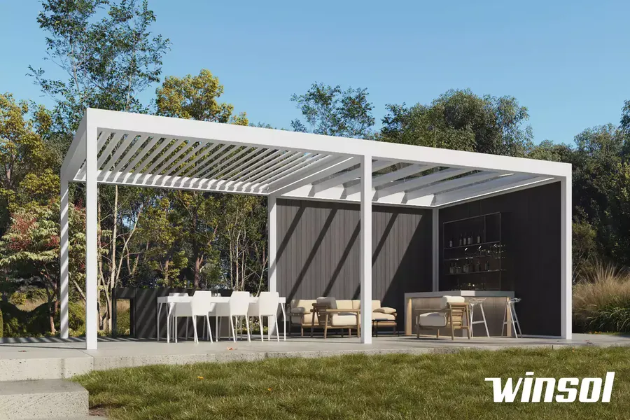 Pergola bioclimatique en aluminium blanc aménagée en espace extérieur lounge avec table, canapé et bar.
