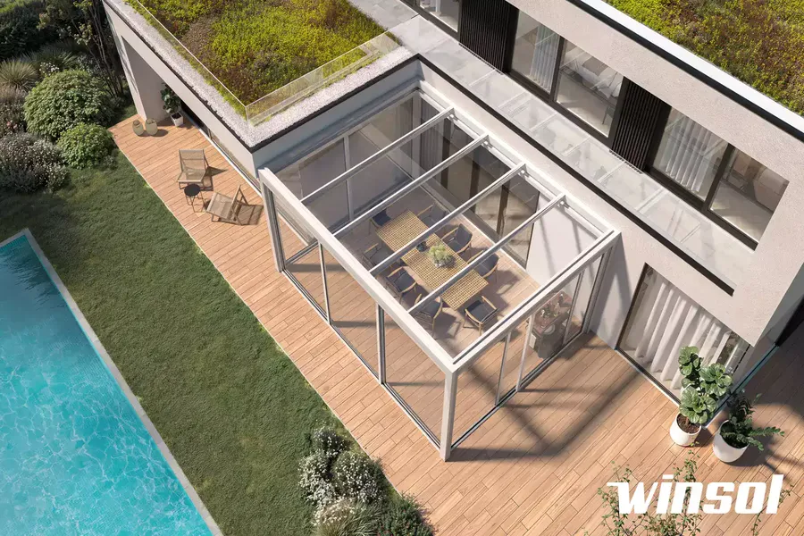 Pergola contemporaine blanche aménagée en pool house avec salon et bar, installée près d'une piscine.