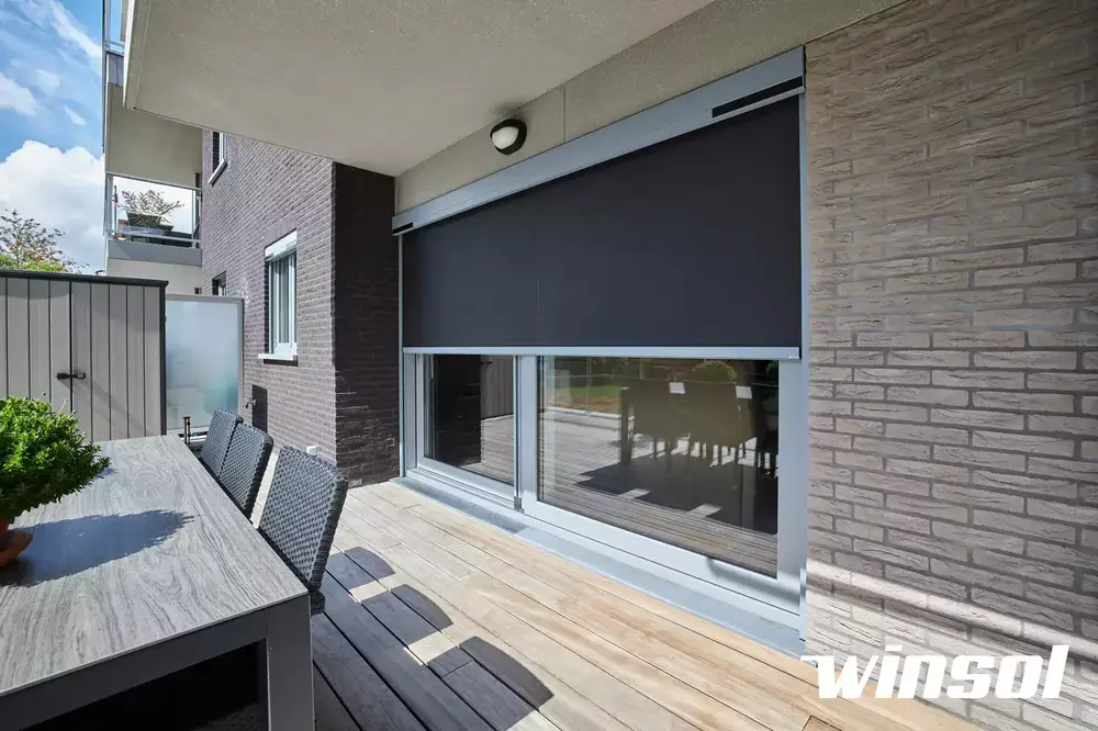 Store anti-chaleur noir sur une baie vitrée avec façade en briques apparentes assurant un ombrage discret