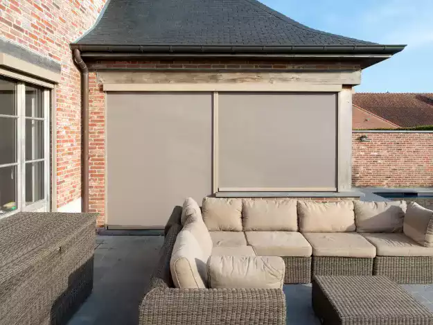 Stores anti chaleur à Pau protégeant un salon de jardin sur terrasse en bois, sous une extension de maison en briques.