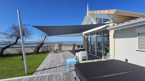 Voile d'ombrage rectangulaire gris foncé installée sur une grande terrasse en bois de maison en bord de mer