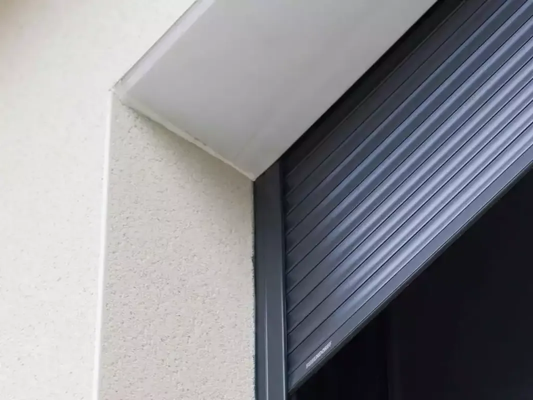 Gros plan sur une installation de volets roulants traditionnels gris anthracite sur une façade blanche.